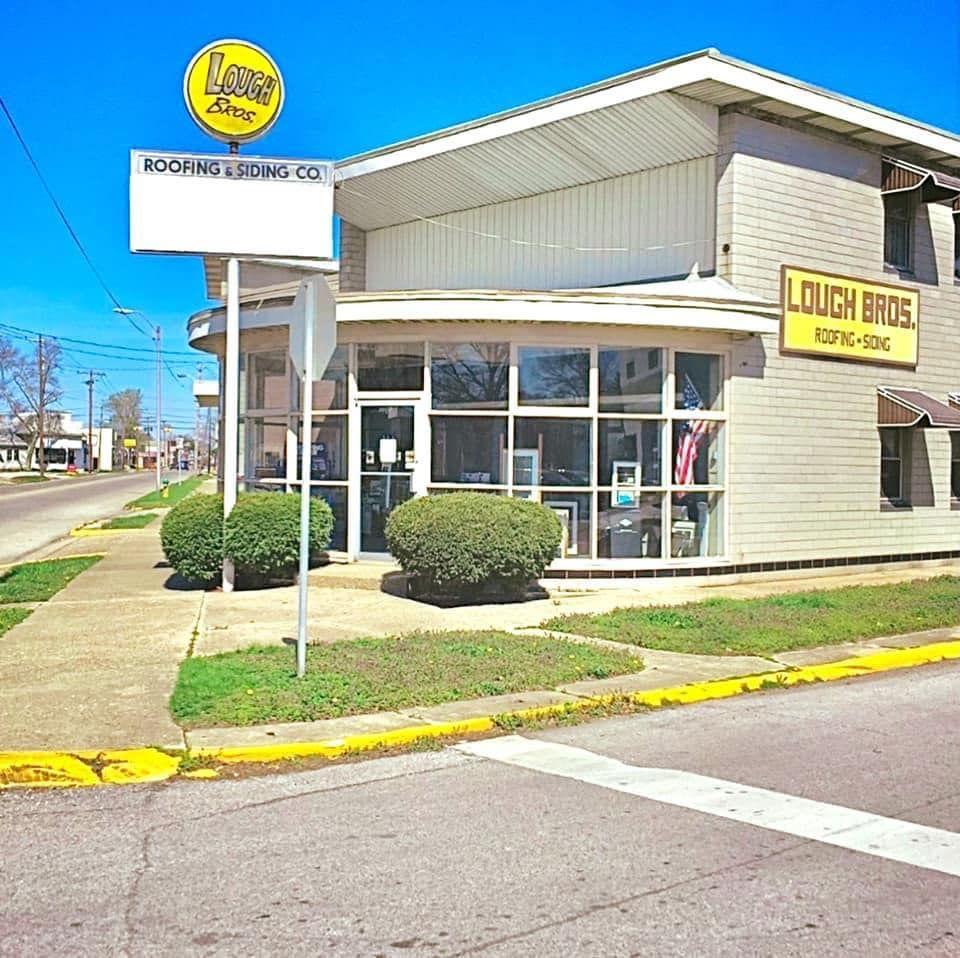 Corner view of a roofing and siding company building with signage and large front windows.