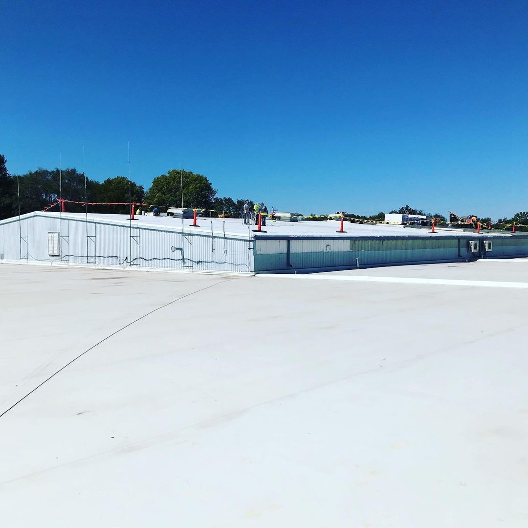 Expansive industrial rooftop with safety cones and workers under a clear blue sky.