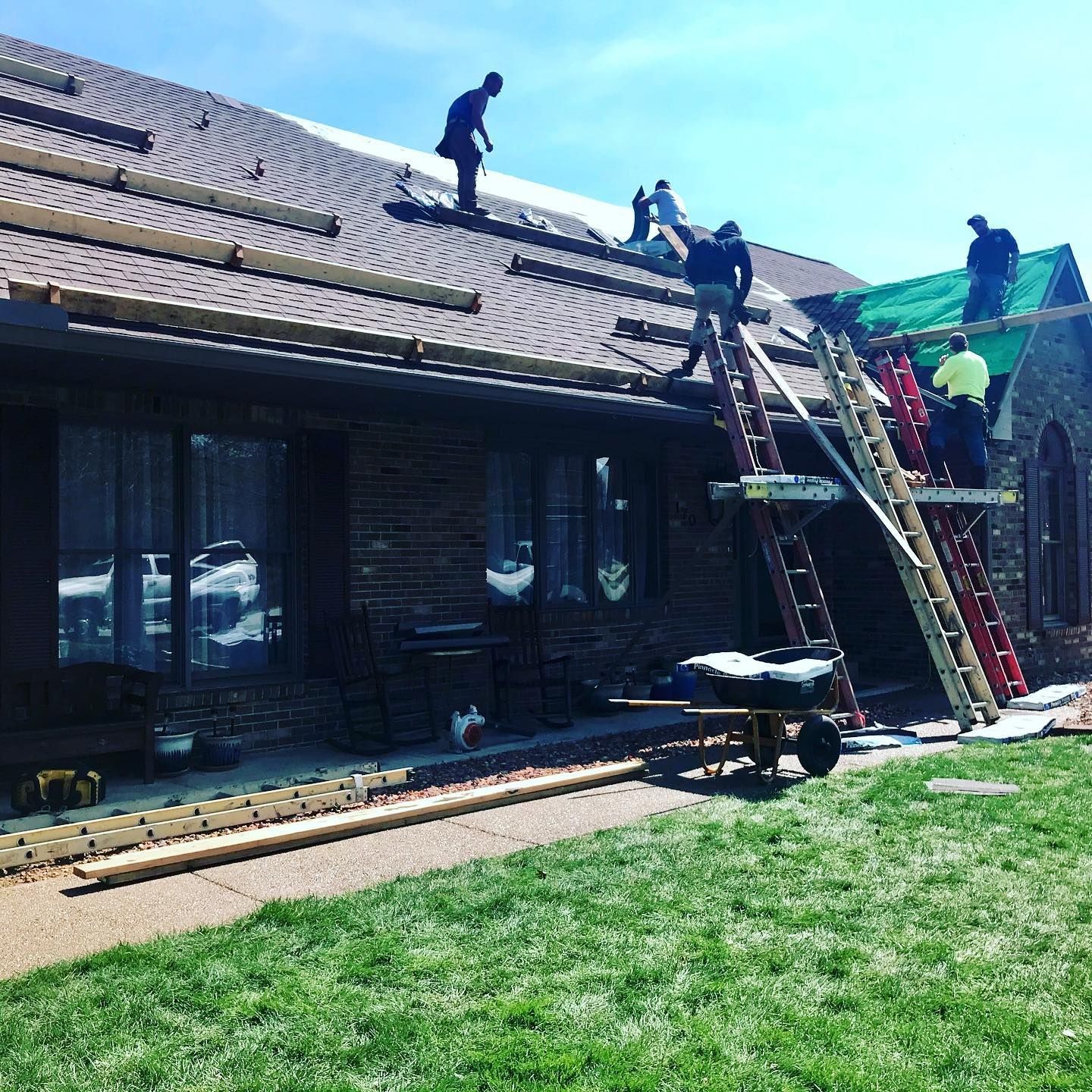 Construction workers on ladders repairing a roof with wooden planks and tools, sunny day.