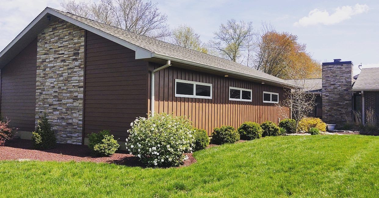 Suburban home with brown siding, stone accents, and lush green lawn under clear sky.